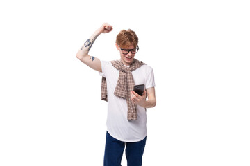 young joyful European red-haired guy in glasses looks into the phone