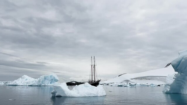 retro style sailing schooner during the huge iceberg in the Antarctic peninsula at the South Pole, waves of the southern ocean in cloudy weather