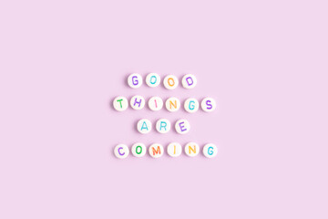 Good things are coming. Quote made of white round beads with multicolored letters on a purple...