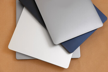 Different modern laptops on brown background, top view