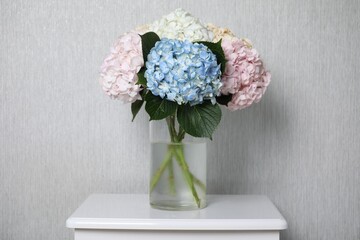 Beautiful hydrangea flowers in vase on white bedside table near light gray wall