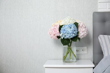 Beautiful hydrangea flowers in vase on white bedside table indoors, space for text