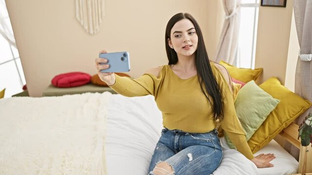 A young hispanic woman takes a selfie in her cozy bedroom, showcasing a casual style and modern living.