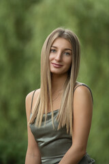 Naklejka premium Portrait of a young beautiful blonde girl in a green dress in a city park.