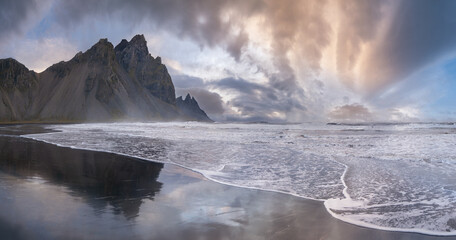 Sunrise Stokksnes cape sea beach and Vestrahorn Mountain with its reflection on wet black volcanic...