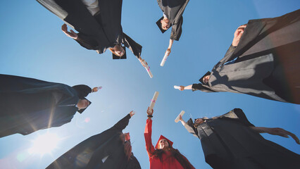College graduates join hands with diplomas standing in a circle.