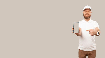 Banner size shot of a young bearded delivery man pointing at a phone he is holding.