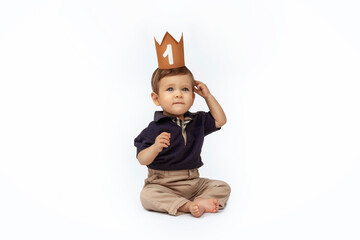 Bebé de un año sentado delante de un fondo blanco, celebrando su primer año con una corona.