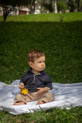 Bebé de un año sentado sobre una manta blanca en un parque en un día soleado