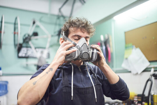 Portrait of a latin young worker removing a respiratory protection mask, as he finishes a spray painting job in his workshop. Health protection in industrial work. Real people working.