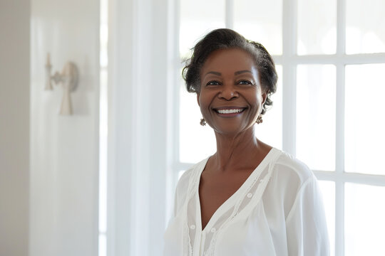 Beautiful 60-year-old African American woman, standing in white blouse against the background of a white bathroom and big windows