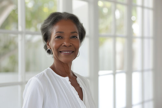 Beautiful 60-year-old African American woman, standing in white blouse against the background of a white bathroom and big windows
