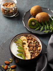 Granola or muesli with yogurt, banana and kiwi on a dark background with napkin.