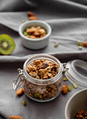 Homemade granola in a jar on a dark linen background with nuts and fruits close up.