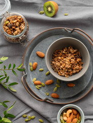 Homemade granola in a jar and bowl on a dark linen background with nuts and fruits.