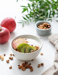 Healthy breakfast. Homemade granola or muesli with apple, kiwi and nuts in a bowl on a white background.