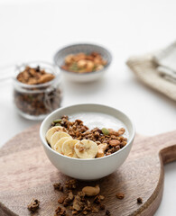 Baked granola with yogurt and banana on a cutting board on a white table.