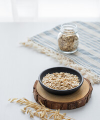 Oatmeal in a plate and in a jar on a napkin on a white textured table in front of the kitchen window.