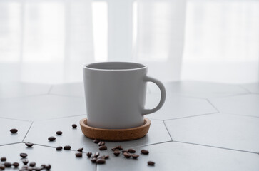 A cup of black coffee on a trendy gray tile background with coffee beans and morning light from the...