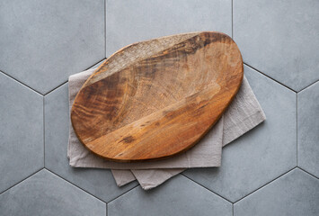 Empty wooden cutting board with napkin on gray ceramic tile in hexagon shape.