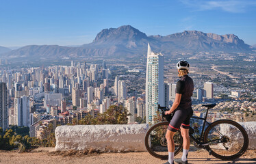 Woman cyclist riding a bike with beautiful view on Benidorm,Costa Blanca,Spain.Woman cyclist wearing cycling kit and helmet.Sports motivation image.Cycling through stunning Spanish mountain landscape.