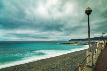The landscape of Varazze, Liguria, Italy in winter, during a rainy day, with dramatic clouded sky. Blurred blue waters of mediterranean sea on the left. Dark clouds on top. - obrazy, fototapety, plakaty