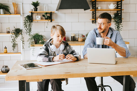 family dad young man with phone and son teenage cute boy with tablet and headphones doing homework sit at table in cosy apartment, quality time with your family, gadget addicted, education