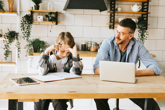family dad young man with phone and son teenage cute boy with tablet and headphones doing homework sit at table in cosy apartment, quality time with your family, gadget addicted, education
