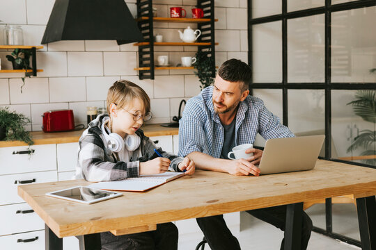 family dad young man with phone and son teenage cute boy with tablet and headphones doing homework sit at table in cosy apartment, quality time with your family, gadget addicted, education