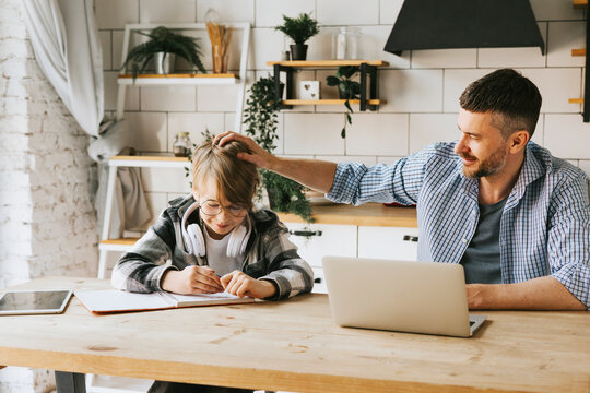 family dad young man with phone and son teenage cute boy with tablet and headphones doing homework sit at table in cosy apartment, quality time with your family, gadget addicted, education