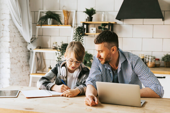 family dad young man with phone and son teenage cute boy with tablet and headphones doing homework sit at table in cosy apartment, quality time with your family, gadget addicted, education - Powered by Adobe