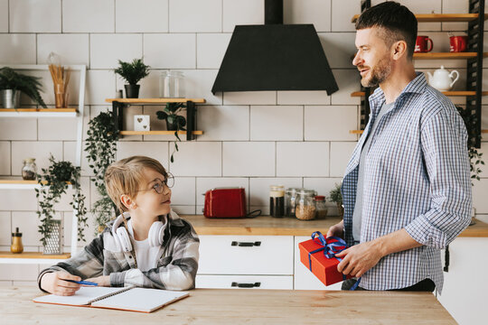 family dad young man and son teenage cute boy doing homework sit at table in cosy apartment, quality time with your family, dad gives the child a gift