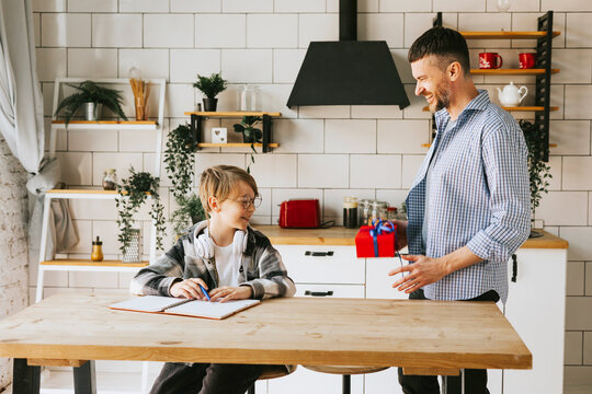 family dad young man and son teenage cute boy doing homework sit at table in cosy apartment, quality time with your family, dad gives the child a gift