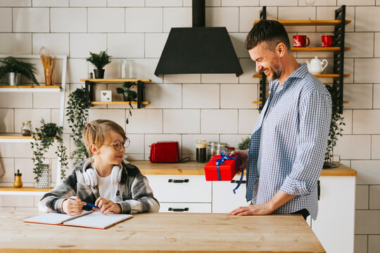 family dad young man and son teenage cute boy doing homework sit at table in cosy apartment, quality time with your family, dad gives the child a gift