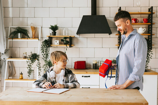 family dad young man and son teenage cute boy doing homework sit at table in cosy apartment, quality time with your family, dad gives the child a gift