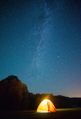 night shot capturing a yellow tent lit up from within, and the awe-inspiring Milky Way and stars in...