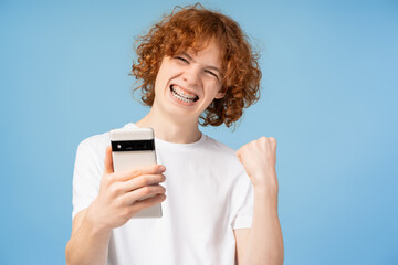 Overjoyed red haired teenager holding mobile screaming, shopping online with sales