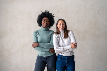 Portrait photo of a two interracial women smiling at camera while standing against a studio...
