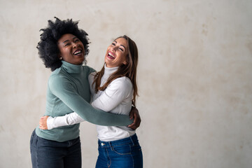 Two best friends smiling while embracing each other in a studio. Happy young women enjoying...