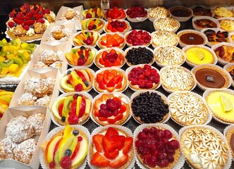 bright french pastries in a baker window, with choux à la creme, flan, tropezienne, and colorfull fruits tarts