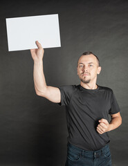 Young serious man holding empty white sheet of paper under his head