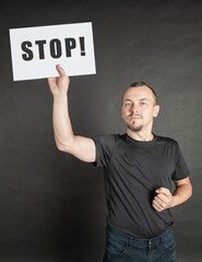 Young serious man holding white sheet of paper stop sign under his head