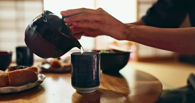 Person, hands and tea pot for pouring hot water at table for meal, Chinese tradition or eating at home. Closeup of people with food, snack and drinking with chop sticks, mug or warm cup to drink