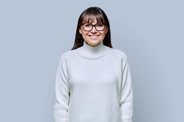 Middle-aged beautiful smiling woman in white sweater on gray studio background