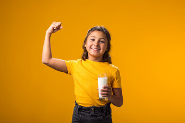 Smiling child girl holding glass of milk and showing strenght gesture. Nutrition and health concept