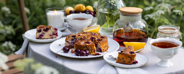 Elegant glamour table setting outdoor in the garden. White porcelain cups, teapot with herbal tea, homemade cherry sweet pie. Family tradition, beautiful place outside. Flower meadow, candles. Banner