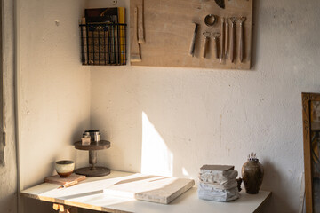 Warm sunlight bathes a tidy workshop corner, highlighting an array of ceramic tools, clay pieces,...