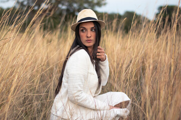 Mujer con sombrero y vestido blanco en un prado rodeada de naturaleza