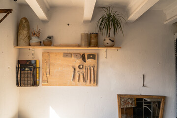 A cozy artisan's corner with a variety of pottery tools lined up on a pegboard, ceramic works on a shelf, and a refreshing plant adding a touch of greenery