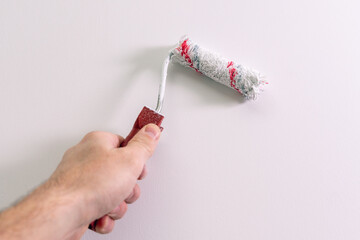 A man's hand paints a wall white with a paint roller